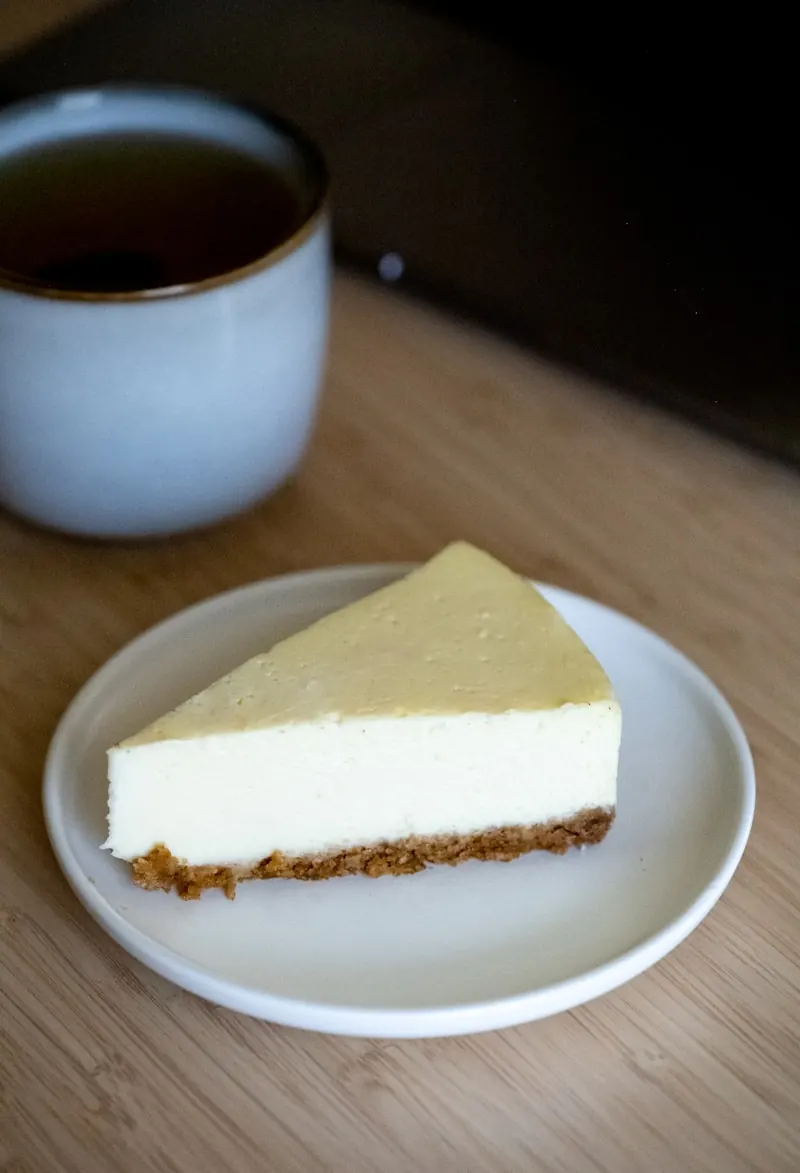 Part de cheesecake spéculoos sur une assiette blanche, texture crémeuse en pleine lumière.