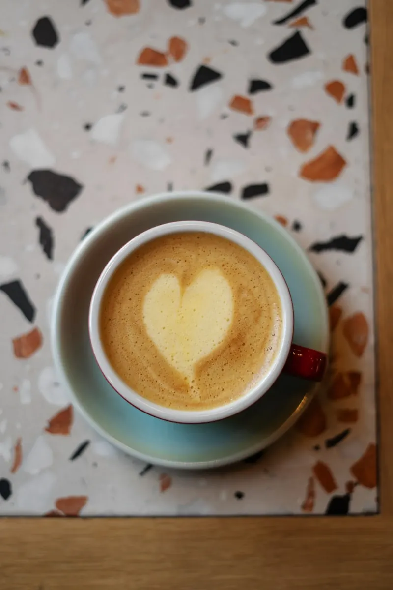 Latte art en cœur dans une tasse blanche, vue de dessus sur surface claire.